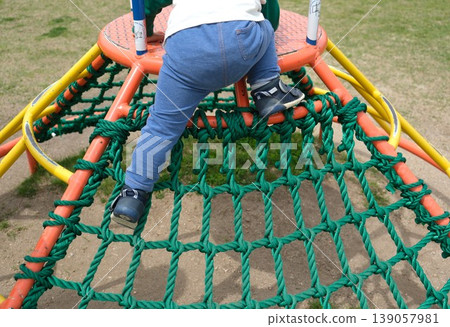 The back view of a child climbing to the top of an athletic playground structure. 139057981