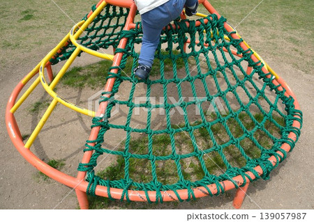 A child's back as they climb to the top of an athletic playground structure. A child's back as they climb to the top of an athletic playground structure. 139057987