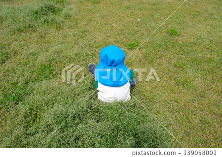 A child wearing a light blue hat sits in the middle of the grass. A child wearing a light blue hat sits in the middle of the grass. 139058001