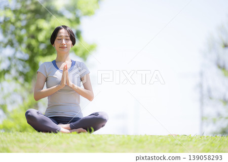 一位女性在綠樹環繞的公園裡練習瑜珈;冥想和健康的生活方式;放鬆和正念的意象。 一位女性在綠樹環繞的公園裡練習瑜珈;冥想和健康的生活方式;放鬆和正念的意象。 139058293