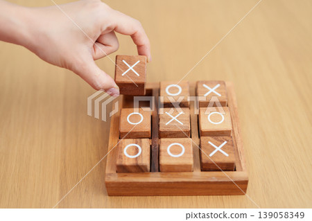Hand holding and playing wooden block of tic tac toe game. A completed game of noughts and crosses or Xs and Os game. Challenge, Competition, winning, tactic, strategy and recreation concepts Hand holding and playing wooden block of tic tac toe game. A completed game of noughts and crosses or Xs and Os game. Challenge, Competition, winning, tactic, strategy and recreation concepts 139058349