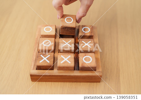 Hand holding and playing wooden block of tic tac toe game. A completed game of noughts and crosses or Xs and Os game. Challenge, Competition, winning, tactic, strategy and recreation concepts Hand holding and playing wooden block of tic tac toe game. A completed game of noughts and crosses or Xs and Os game. Challenge, Competition, winning, tactic, strategy and recreation concepts 139058351