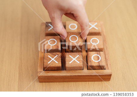 Hand holding and playing wooden block of tic tac toe game. A completed game of noughts and crosses or Xs and Os game. Challenge, Competition, winning, tactic, strategy and recreation concepts Hand holding and playing wooden block of tic tac toe game. A completed game of noughts and crosses or Xs and Os game. Challenge, Competition, winning, tactic, strategy and recreation concepts 139058353