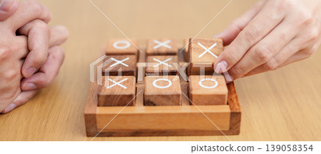 Hand holding and playing wooden block of tic tac toe game. A completed game of noughts and crosses or Xs and Os game. Challenge, Competition, winning, tactic, strategy and recreation concepts 139058354