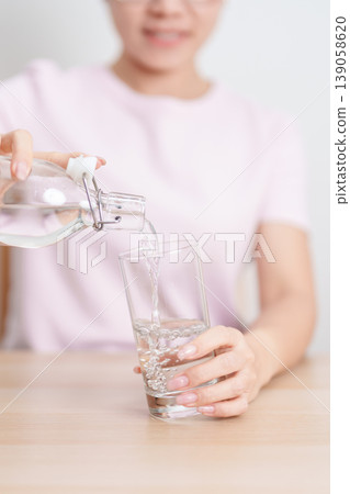 Healthy woman pour clean mineral water into glass at home, female drink pure water for hydration and wellness, fresh skin care, daily routine water intake, Refreshment and lifestyle concept Healthy woman pour clean mineral water into glass at home, female drink pure water for hydration and wellness, fresh skin care, daily routine water intake, Refreshment and lifestyle concept 139058620