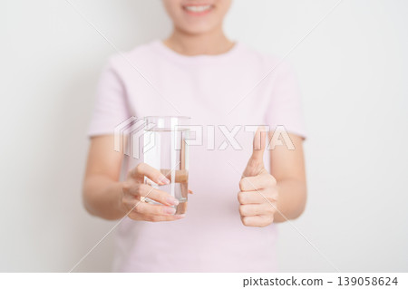 Healthy woman hold glass of clean mineral water and show thumbs up, female drink pure water for hydration and wellness, fresh skin care, daily routine water intake, Refreshment and lifestyle concept Healthy woman hold glass of clean mineral water and show thumbs up, female drink pure water for hydration and wellness, fresh skin care, daily routine water intake, Refreshment and lifestyle concept 139058624