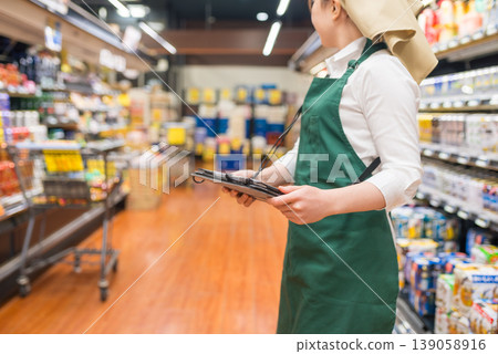 A woman in an apron walks down a supermarket aisle. A woman in an apron walks down a supermarket aisle. 139058916