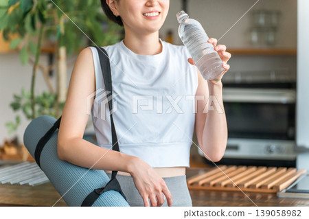 Asian woman hydrating with bottled mineral water after home training Asian woman hydrating with bottled mineral water after home training 139058982