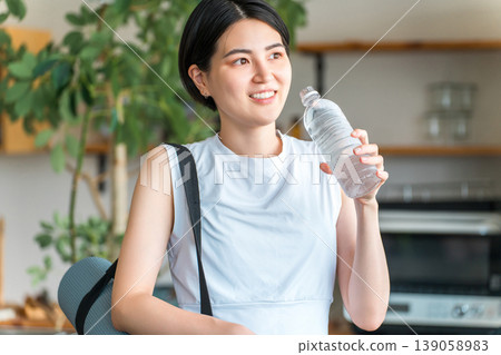 Asian woman hydrating with bottled mineral water after home training Asian woman hydrating with bottled mineral water after home training 139058983