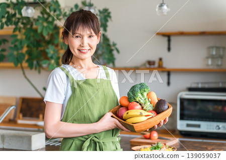Middle-aged Asian woman/housewife wearing an apron holding vegetables in the kitchen 139059037