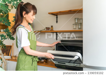 A woman using a microwave in the kitchen (cooking service, housekeeping service, housekeeper, helper) A woman using a microwave in the kitchen (cooking service, housekeeping service, housekeeper, helper) 139059102
