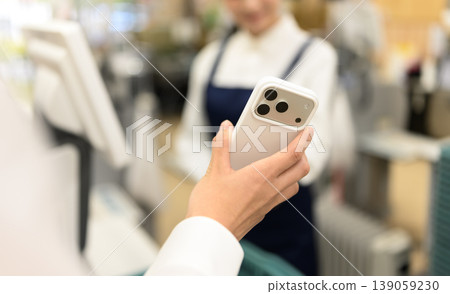 一位女士在收銀台用智慧型手機付款。 一位女士在收銀台用智慧型手機付款。 139059230