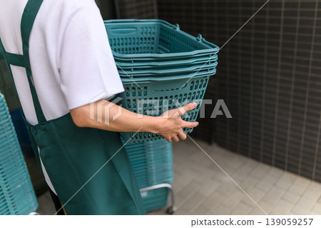 A male shop assistant carries a shopping basket. A male shop assistant carries a shopping basket. 139059257
