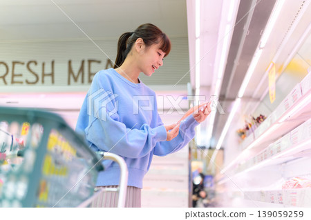A woman chooses products while looking at her smartphone. A woman chooses products while looking at her smartphone. 139059259