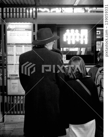 A monochrome street photo of a train station and the back of a person. 139059331