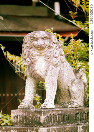 Stone statues of guardian lions at a shrine against a backdrop of fresh greenery (guardian lion photo) 139060080
