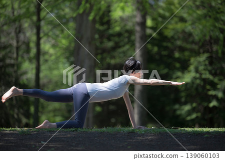 A woman's training and yoga fitness routine in a lush green forest, focusing on core strength with a bird dog. A woman's training and yoga fitness routine in a lush green forest, focusing on core strength with a bird dog. 139060103