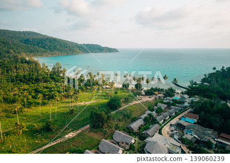 Aerial view of a tropical island resort village nestled between lush forest and the beach. Aerial view of a tropical island resort village nestled between lush forest and the beach. 139060239