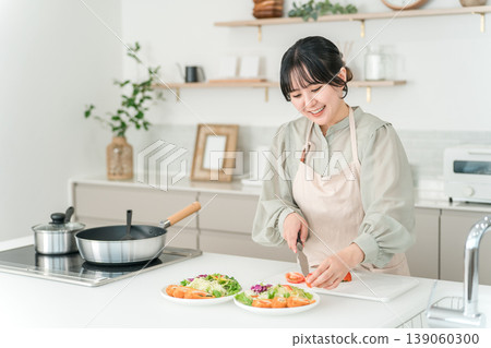年輕的亞裔女子穿著圍裙在廚房做飯 年輕的亞裔女子穿著圍裙在廚房做飯 139060300