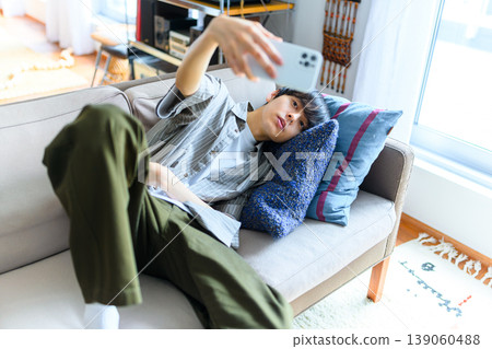 A young man taking a selfie on a sofa. 139060488