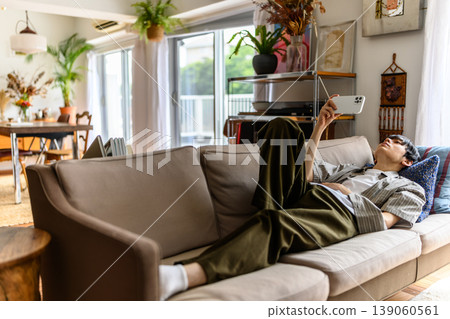 A man sits on a sofa in a spacious living room, looking at his smartphone. A man sits on a sofa in a spacious living room, looking at his smartphone. 139060561