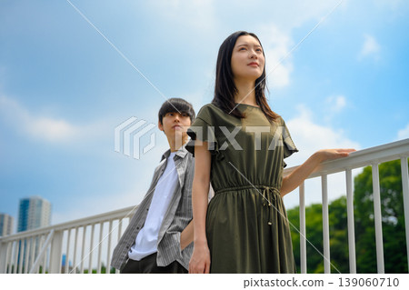 A man and a woman leaning against a railing, against a blue sky. 139060710