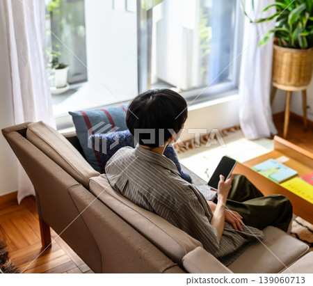 The back view of a man sitting on a sofa and looking out the window. 139060713
