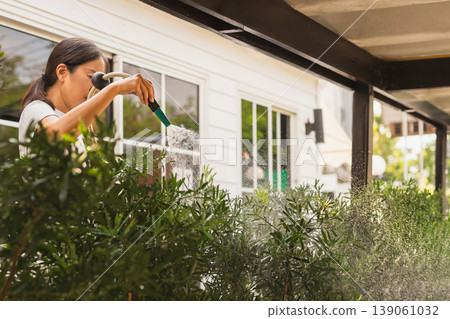 Woman waters lush garden bushes outside in the morning. 139061032
