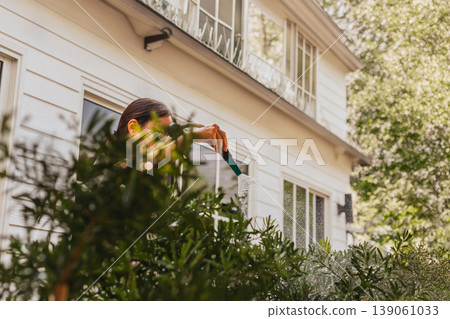 Woman waters lush garden bushes outside in the morning. Woman waters lush garden bushes outside in the morning. 139061033