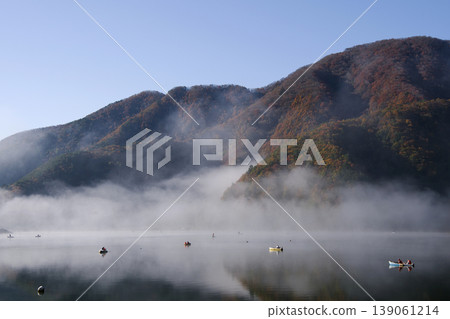 秋季的精進湖籠罩在晨霧中。秋色斑斕的山巒和漁船構成了一幅如夢似幻、令人印象深刻的景象。 139061214