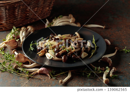 Fried shimeji mushrooms with thyme and garlic on a black plate. 139062565