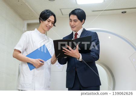 A businessman and a doctor maintaining a hospital's CT scanner. Filming assistance provided by: Denpa Gakuen Educational Foundation, Tokyo Electronics College. A businessman and a doctor maintaining a hospital's CT scanner. Filming assistance provided by: Denpa Gakuen Educational Foundation, Tokyo Electronics College. 139062626