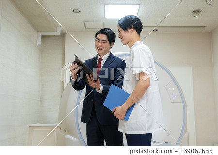 A businessman and a doctor maintaining a hospital's CT scanner. Filming assistance provided by: Denpa Gakuen Educational Foundation, Tokyo Electronics College. A businessman and a doctor maintaining a hospital's CT scanner. Filming assistance provided by: Denpa Gakuen Educational Foundation, Tokyo Electronics College. 139062633