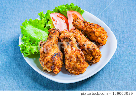 Deep-fried chicken wings with lettuce and tomato as a side dish, served on a white plate – a home-style meal. 139063059