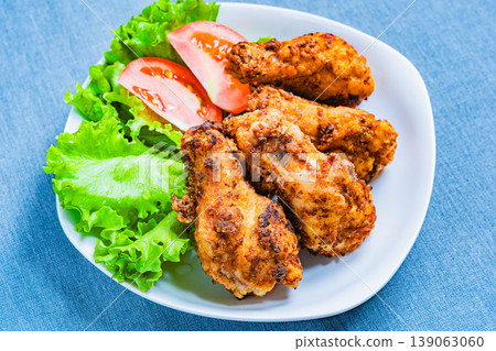Deep-fried chicken wings with lettuce and tomato as a side dish, served on a white plate – a home-style meal. Deep-fried chicken wings with lettuce and tomato as a side dish, served on a white plate – a home-style meal. 139063060
