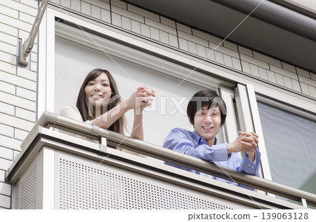 A young couple looking at us from their balcony A young couple looking at us from their balcony 139063128