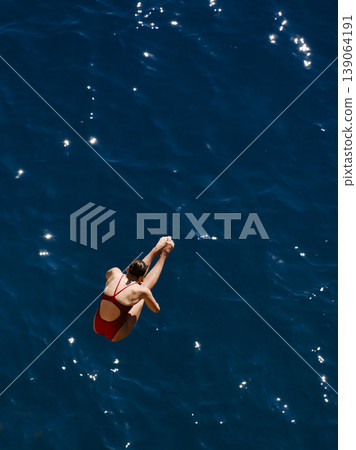 a professional female diver is jumping off a cliff into the sea a professional female diver is jumping off a cliff into the sea 139064191