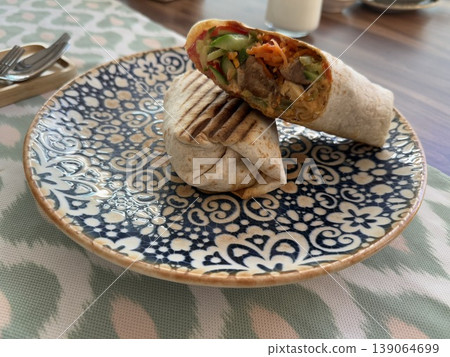 Grilled chicken wrap with vegetables on patterned plate offers delicious lunchtime concept Grilled chicken wrap with vegetables on patterned plate offers delicious lunchtime concept 139064699