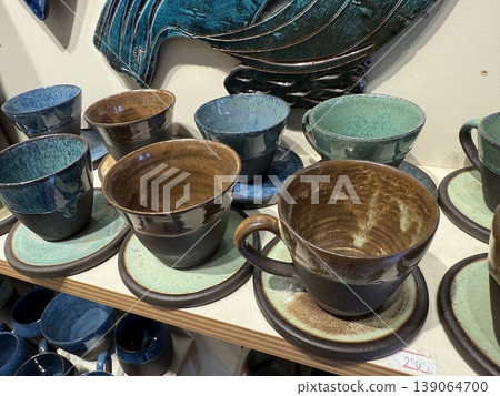 Ceramic cups and saucers displayed on shelf showcasing artisanal craftsmanship and glaze styles Ceramic cups and saucers displayed on shelf showcasing artisanal craftsmanship and glaze styles 139064700