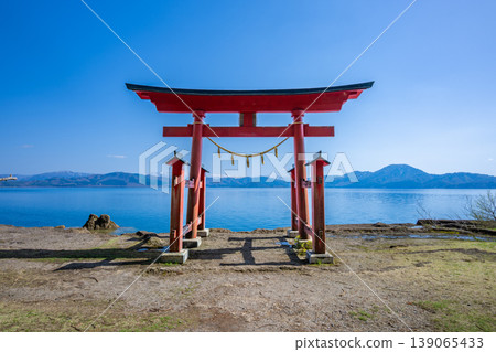 The torii gate of Gozaishi Shrine, standing on the shores of Lake Tazawa in Akita, and the breathtaking view of Lake Tazawa's blue waters reflected on the lake's surface. The torii gate of Gozaishi Shrine, standing on the shores of Lake Tazawa in Akita, and the breathtaking view of Lake Tazawa's blue waters reflected on the lake's surface. 139065433