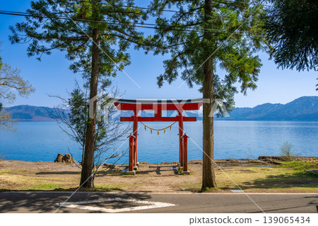 The torii gate of Gozaishi Shrine, standing on the shores of Lake Tazawa in Akita, and the breathtaking view of Lake Tazawa's blue waters reflected on the lake's surface. The torii gate of Gozaishi Shrine, standing on the shores of Lake Tazawa in Akita, and the breathtaking view of Lake Tazawa's blue waters reflected on the lake's surface. 139065434