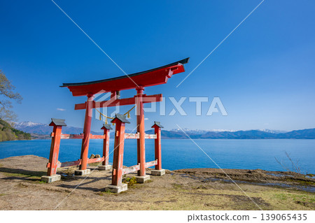 The torii gate of Gozaishi Shrine, standing on the shores of Lake Tazawa in Akita, and the breathtaking view of Lake Tazawa's blue waters reflected on the lake's surface. The torii gate of Gozaishi Shrine, standing on the shores of Lake Tazawa in Akita, and the breathtaking view of Lake Tazawa's blue waters reflected on the lake's surface. 139065435