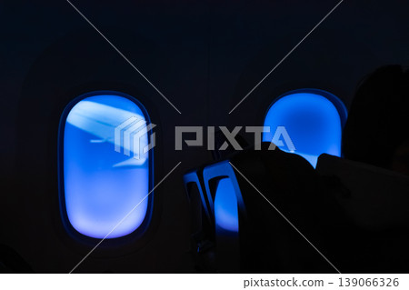 The dimmed blue light of the aircraft's windows and the silhouette of its wings. The dimmed blue light of the aircraft's windows and the silhouette of its wings. 139066326