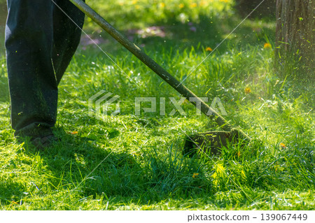 professional garden service at work. lawn care concept. cutting an mowing grass in the park. spring summer season. backlit gardening scene. grass ground view for design professional garden service at work. lawn care concept. cutting an mowing grass in the park. spring summer season. backlit gardening scene. grass ground view for design 139067449