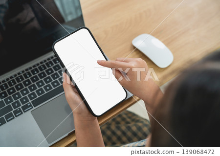 Close-Up View of a Person Interacting with a Smartphone Screen in an Office Setting with Laptop and Mouse on a Wooden Desk Close-Up View of a Person Interacting with a Smartphone Screen in an Office Setting with Laptop and Mouse on a Wooden Desk 139068472