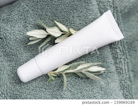 White blank eye cream tube mockup with green leaves on sage green towel. Cosmetic product packaging White blank eye cream tube mockup with green leaves on sage green towel. Cosmetic product packaging 139069189