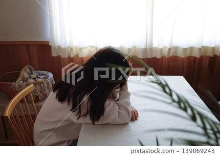一位頭髮蓬亂、身穿家居服的女子無精打采地低著頭。 一位頭髮蓬亂、身穿家居服的女子無精打采地低著頭。 139069243