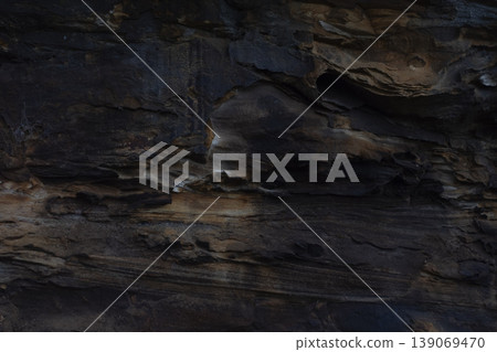 Dark natural layered rock formation with textured geological patterns Dark natural layered rock formation with textured geological patterns 139069470