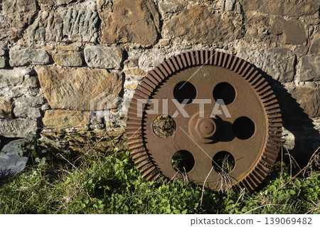 Old rusty gear leaning against stone wall Old rusty gear leaning against stone wall 139069482
