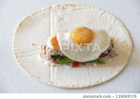 Tortilla wrap with mozzarella, vegetables, tuna, and fried egg on white background Tortilla wrap with mozzarella, vegetables, tuna, and fried egg on white background 139069576